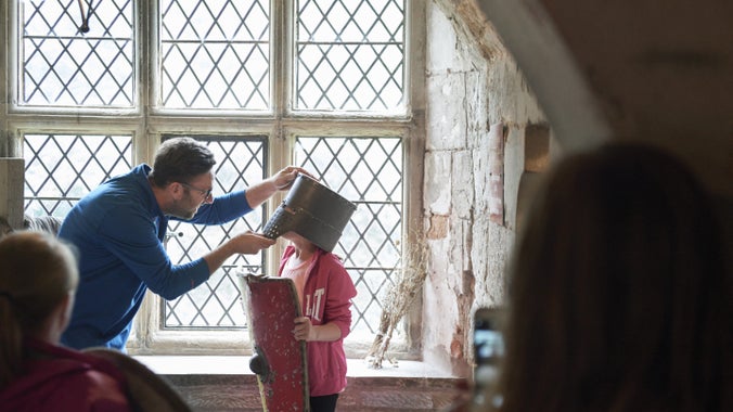 Oedolyn yn helpu plentyn i wisgo dillad canol oesol y tu mewn i Gastell y Waun, Wrecsam, Cymru.